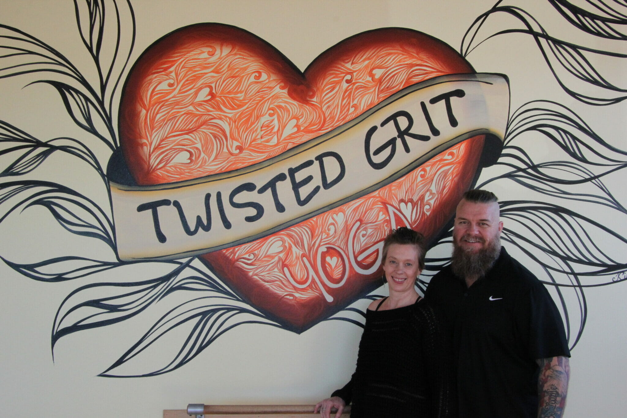 Owners Amy and Scott standing in front of a Twisted Grit Yoga mural in their studio